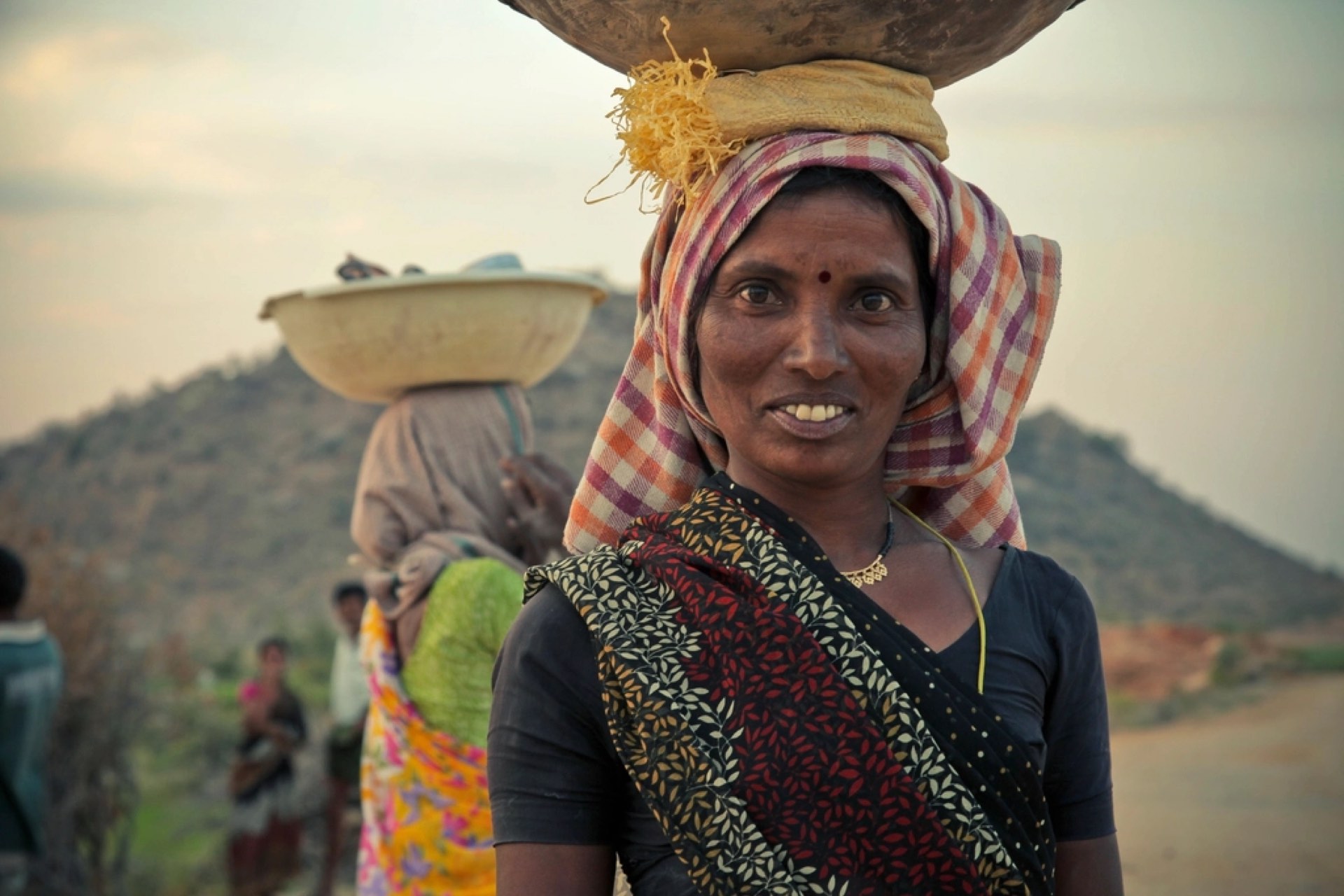 A smiling woman carrying a basket on her head