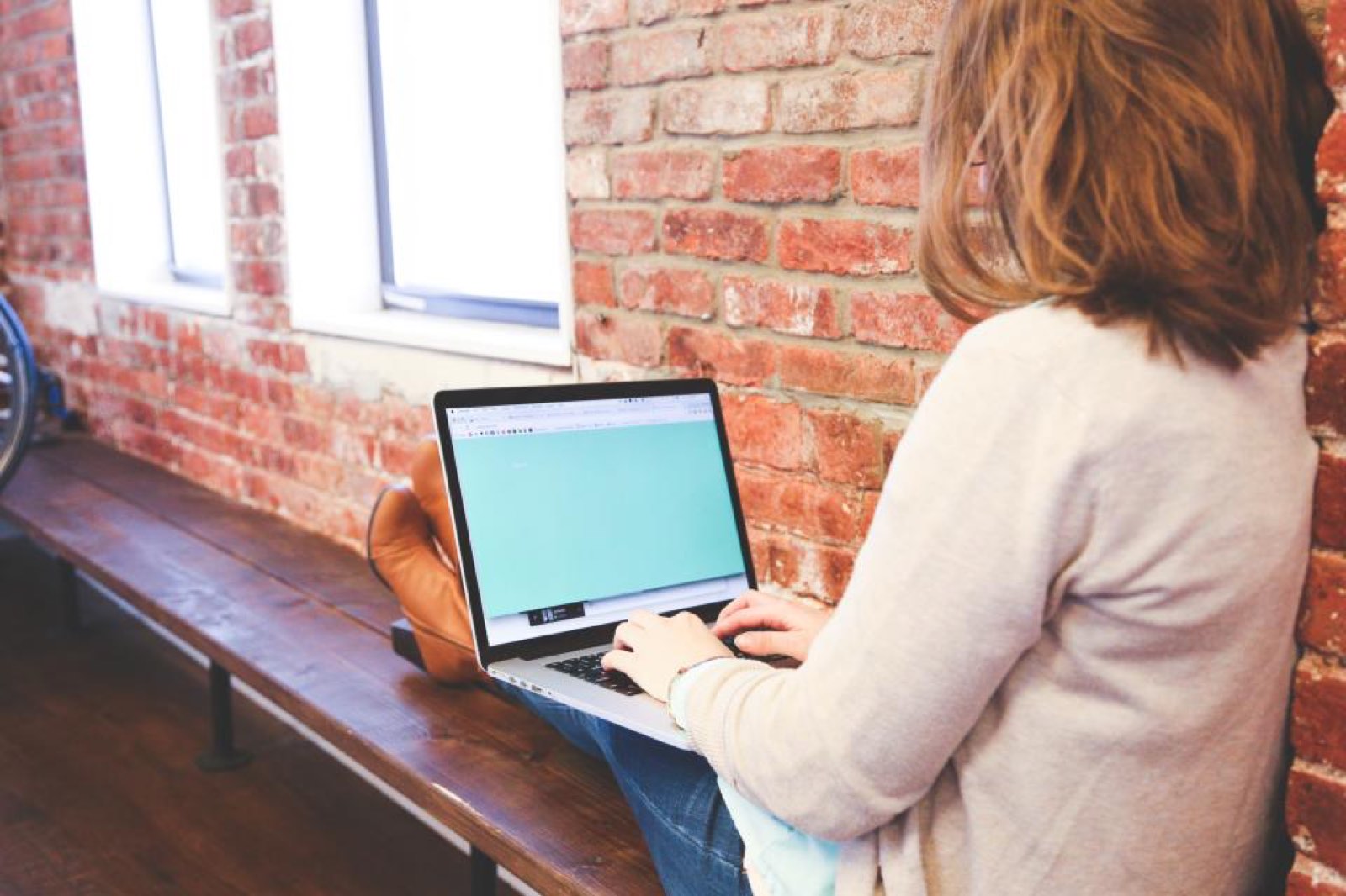 A woman working on a laptop by a brick wall
