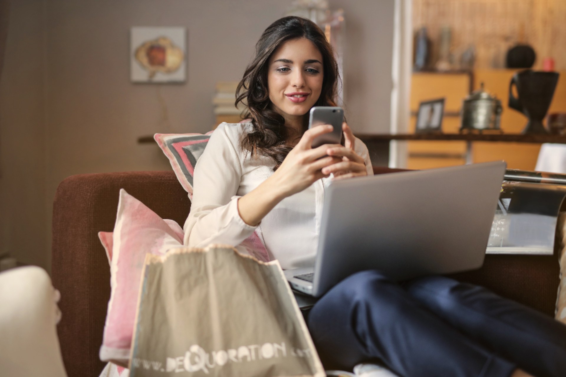 A smiling woman working on her laptop and phone at home